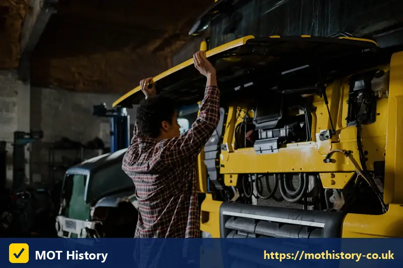Mechanic checking under the cab of a yellow lorry - class 5 mot