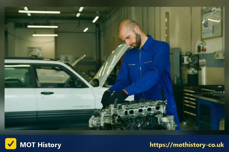 Mechanic holding an engine cylinder head beside a car - gasoline check