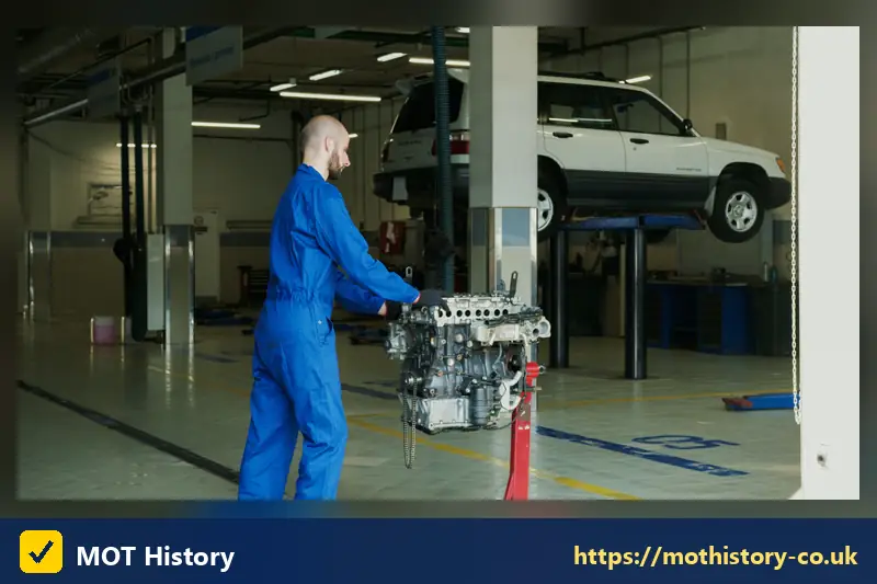 Mechanic carrying an engine in a garage with a car on a lift - has my car been scrapped