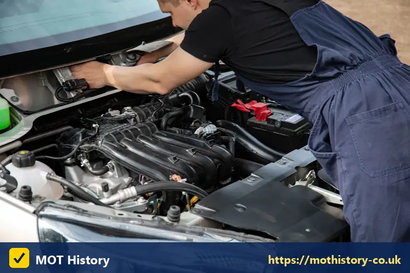 Mechanic reaching into a car engine bay - mot centres northern ireland