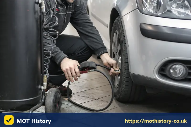 Mechanic inflating a car tyre in a garage - mot early
