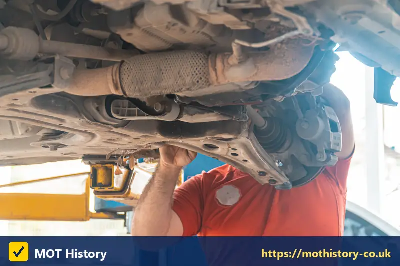 Mechanic underneath a car checking the exhaust and driveshaft - mot test classes