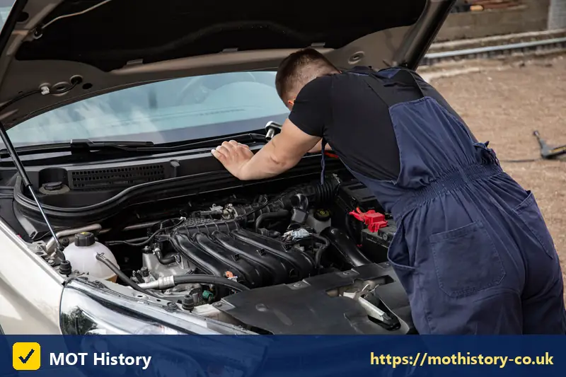 Mechanic in blue overalls inspecting a car engine - new buildings mot centre