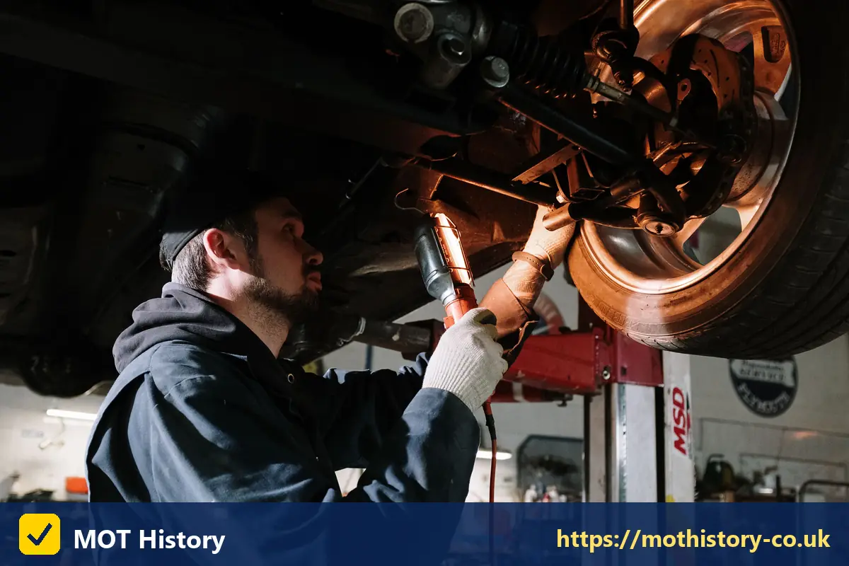 Mechanic inspecting brakes and suspension with a torch - irish mot checker
